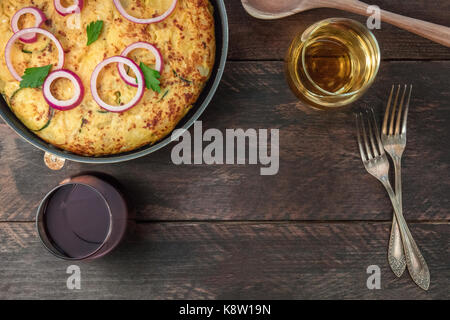 Ein Foto von einem spanischen Tortilla mit Kartoffeln und Zucchini in einem Tortillera, mit Brille von Rot- und Weißwein, und einen Platz für Text Stockfoto