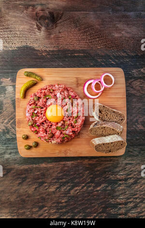 Ein Foto von einem Steak Tartar mit einem rohen Eigelb, Roggenbrot, und lila Zwiebeln, geschossen von oben auf einen dunklen rustikalen Textur mit einem Platz für Text Stockfoto