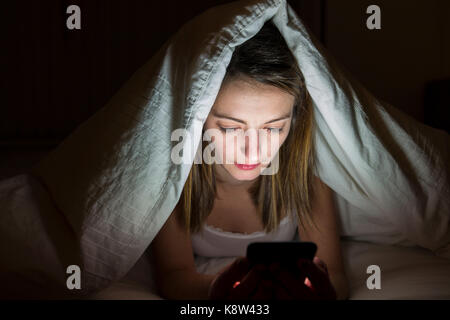 Frau mit Smartphone auf dem Bett in der Nacht Stockfoto
