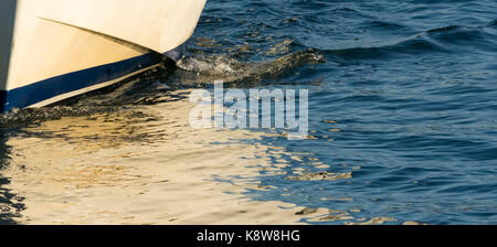 Eine kleine Welle zeigt, wie die weißen Rumpf eines kleinen Bootes Schnitte durch kleine Wellen in der Wasseroberfläche. Stockfoto