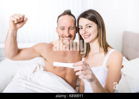Fröhliche Paare herausfinden, Ergebnisse einer Schwangerschaft Test sitzen auf dem Bett Stockfoto