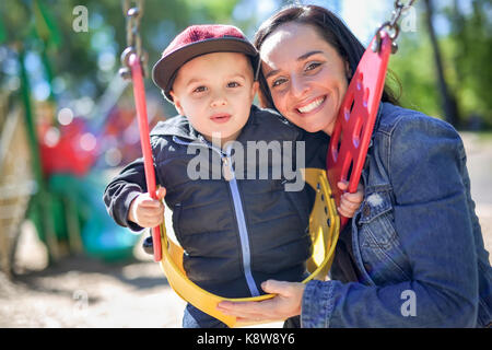 Glückliche Mutter, Sohn auf schwingen in einem Park Stockfoto