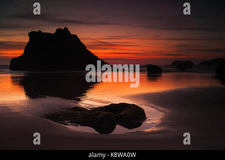 Des Oregon sea Stacks Reflexionen aus dem Zurückweichenden Wellen bei Sonnenuntergang am Bandon Strand. Stockfoto