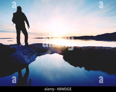 Silhouette Mann auf einer Klippe über dem Meer. Touristische stand alone auf einem Felsen und Meer Horizont Sonnenuntergang. Wanderer die Spiegelung in der Nähe Wasser Pool. Stockfoto