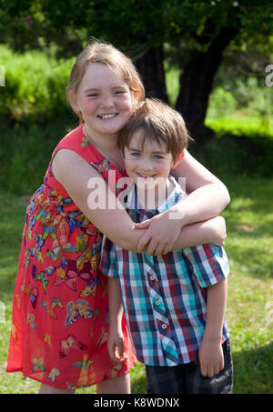 Eine sommersprossige rothaarige Mädchen umarmt sie Braunhaarige Bruder, außerhalb lächelnd in die Sonne Stockfoto
