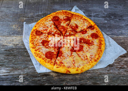 Pizza mit Salami, Pastrami, Schinken und Käse, serviert auf Holztisch. Hausgemachte Pizza mit dicker Kruste Stockfoto