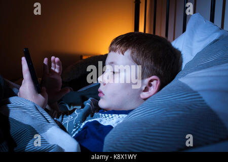 Ein Junge im Bett in der Nacht während der Wiedergabe mit einem Tablet Stockfoto