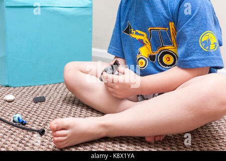 Eine Junge kaukasier Junge saß auf dem Boden in einer häuslichen Umgebung spielen mit LEGO Steinen Stockfoto