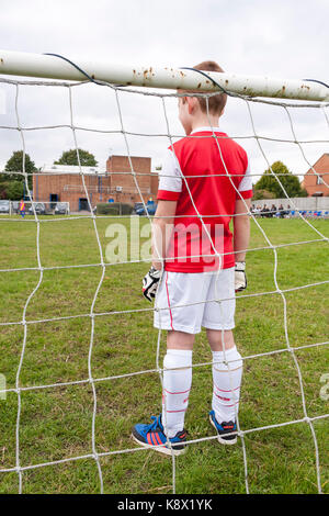 Ein Junge tragen ein Arsenal Kit, im Ziel stehen während eines Fußballspiels von Jungen gespielt wird Stockfoto