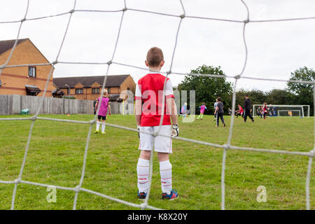 Ein Junge tragen ein Arsenal Kit, im Ziel stehen während eines Fußballspiels von Jungen gespielt wird Stockfoto