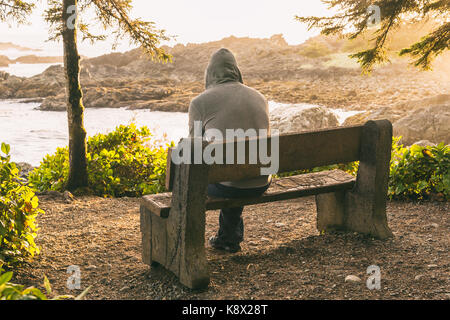 Einsamer Mann sitzt auf der Bank mit Blick auf das Meer auf Vancouver Island bei Sonnenuntergang Stockfoto