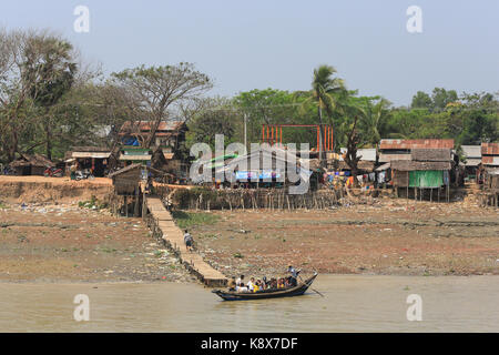 Ein Mann steht beim Rudern ein Boot mit Passagieren auf dem Twante Kanals in einem kleinen Dorf geladen, Myanmar (Birma). Stockfoto