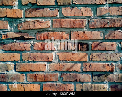 Eine Nahaufnahme eines groben Mauerwerk Wand mit roten ungeschickt Ziegel für die Kreativität, Texturen und Hintergründe gesäumt. Stockfoto