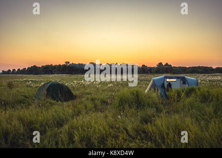 Camping Zelt auf Sommer ländlichen Gebiet mit Wald auf Hintergrund und orange Sonnenuntergang Himmel beim camping urlaub Stockfoto