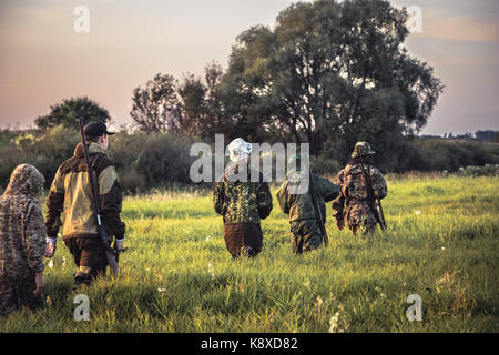 Gruppe Männer Jäger durch hohes Gras auf den ländlichen Bereich bei Sonnenuntergang, während der Jagdsaison Stockfoto