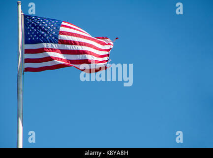 Amerikanische Flagge auf der Pole mit ausgefransten Rand am strahlend blauen Himmel Stockfoto