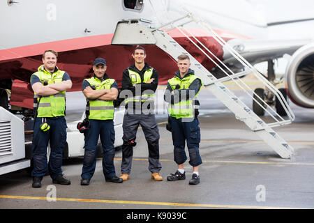 Portrait von Boden Team Stand mit verschränkten Armen gegen Flugzeug Stockfoto