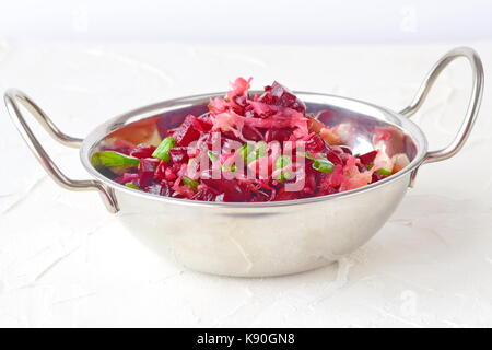 Mischung aus gekochte rote Rüben, Bohnen, Sauerkraut, Essiggurken und grüne Zwiebeln mit Olivenöl und Essig in eine Metallplatte mit den Händen auf einem weißen Hintergrund. Stockfoto