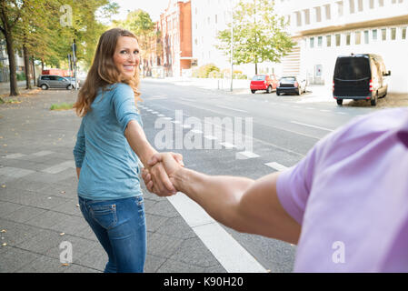 Glückliche Frau ziehen Ihr Mann beim Gehen auf dem Bürgersteig Stockfoto