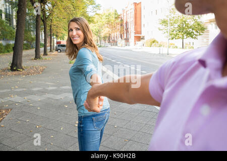Glückliche Frau ziehen Ihr Mann beim Gehen auf dem Bürgersteig Stockfoto