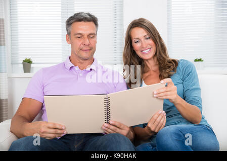 Reifen glückliches Paar sitzt auf der Couch auf Fotoalbum Stockfoto