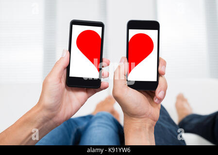 In der Nähe von zwei Menschen die Hände mit Mobiltelefonen, die zwei Hälften des Herzens Form Stockfoto