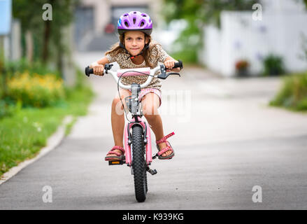 Kinder lernen mit dem Fahrrad auf einer Fahrstraße außerhalb zu fahren. Kleine Mädchen reiten Fahrräder auf Asphalt in der Stadt mit Helm und Schutzkleidung. Stockfoto