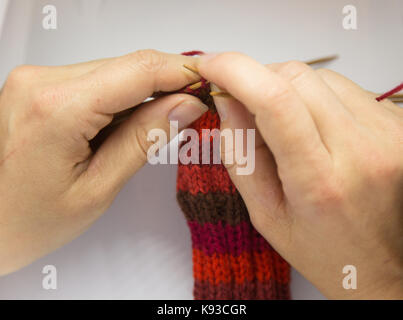 Eine Frau roten Wollsocken stricken. Stricken in der Nähe auf einem weißen Hintergrund. Handwerk. Detailansicht eines Stricken skill. Stockfoto
