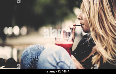 Seitenansicht der Frau mit langen braunen Haaren im Freien sitzen, trinken aus einem Strohhalm. Stockfoto