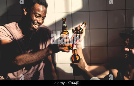 Zwei lächelnde Männer sitzen im Innenbereich, Bierflaschen, toasten. Stockfoto