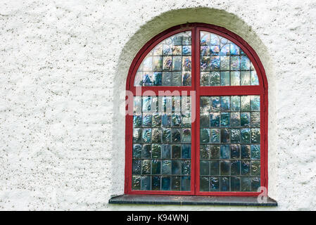 Irisierende Fenster mit roter Rahmen auf weißen Kirche. Stockfoto