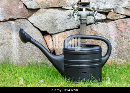 Kunststoff schwarz Bewässerung Topf auf grünem Gras mit Mauer aus Stein und Wasser im Hintergrund tippen. Stockfoto