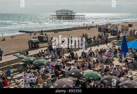 Die Menschen Essen und Trinken in Meer Cafe/Restaurant am Strand von Brighton, East Sussex, England mit alten stillgelegten ruiniert West Pier in backgroun Stockfoto