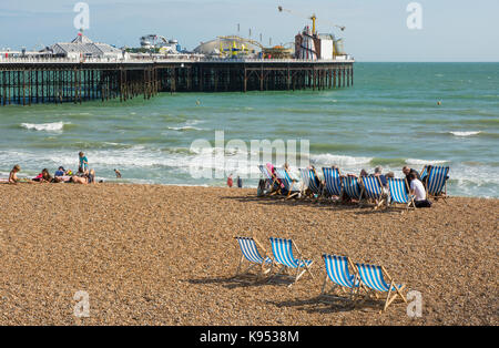 Leute sitzen auf der Kiesstrand an der Brighton, East Sussex, England. Mit Pier im Hintergrund Stockfoto