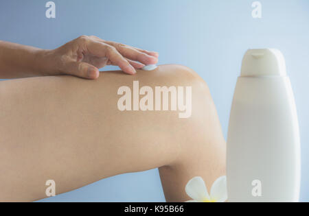 Hand der Frau gelten Lotion auf die Haut der Knie mit Lotion Flasche auf Wand Hintergrund. Stockfoto