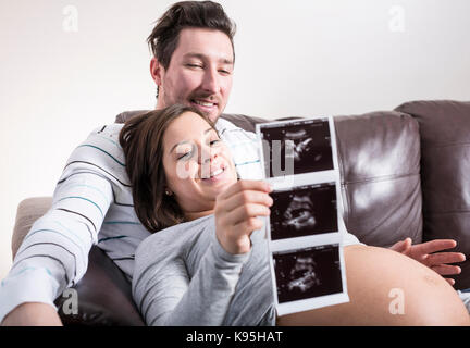 Zukünftige Eltern bei Ultraschall auf der Suche Scan auf dem Sofa Stockfoto