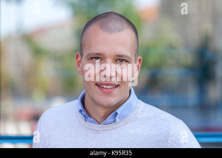 Close up Portrait von hübscher junger Geschäftsmann lächelnd durch die Gebäude in der Stadt. Er lächelt und schaut in die Kamera Stockfoto