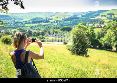 Eine junge Frau reißt die üppigen Peak District Landschaft auf Ihrem Telefon Stockfoto