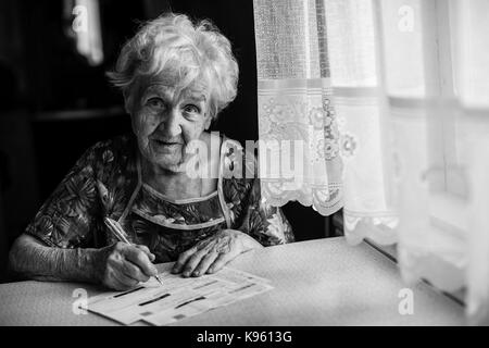 Ältere Frau füllt einen Einzahlungsschein. Schwarz-weiß Portrait. Stockfoto