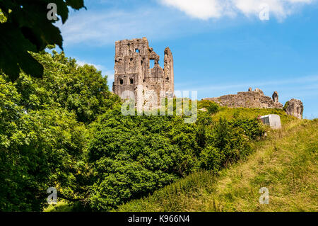 Die romantischen Ruinen des antiken Corfe Castle über einen gefallenen Turm und Mauern auf einem Hügel über einem grünen und bewaldeten steilen Hang halten Stockfoto