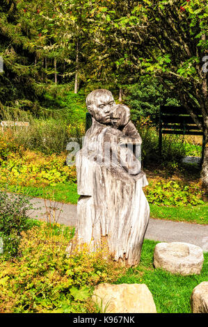 Eine hölzerne Baumstamm geschnitzt in eine Skulptur von einer Frau mit einem Baby, bis Herbst Sonnenlicht in einem Waldgebiet von Visitor Centre Queen's View lit Stockfoto