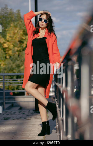 Outdoor portrait einer jungen schönen modischen Frau, im Freien. Das Modell, in einem stilvollen orange Mantel bekleidet, Sonnenbrillen. Das Konzept der Damenmode, urban Lifestyle Stockfoto