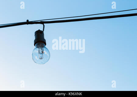 Eine Glühlampe aus, die außen an einem Kabel hängt. Der blaue Himmel im Hintergrund. Stockfoto