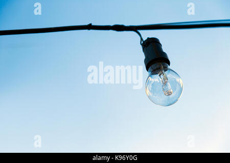 Eine Glühlampe aus, die außen an einem Kabel hängt. Der blaue Himmel im Hintergrund. Stockfoto