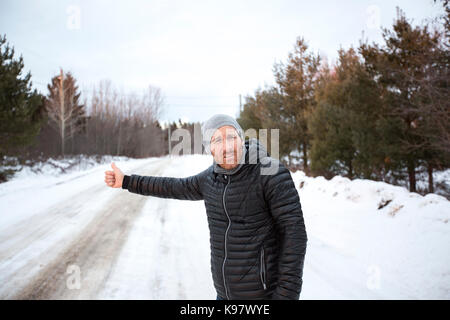 Jungen gutaussehenden Mann in Schwarz Jacke im Winter, stand auf der Autobahn und per Anhalter. Stockfoto