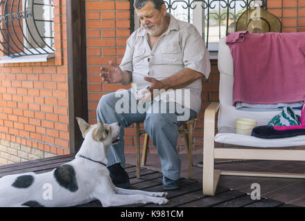 Senior spricht mit Hund in der Nähe von seinem Haus saß Bärtigen Stockfoto