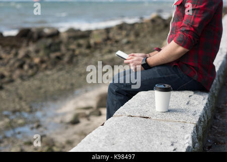 Den mittleren Abschnitt der Mann mit Handy in der Nähe von Strand Stockfoto