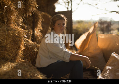Portrait von selbstbewussten jungen Frau sitzt auf der Heuballen auf der Farm Stockfoto