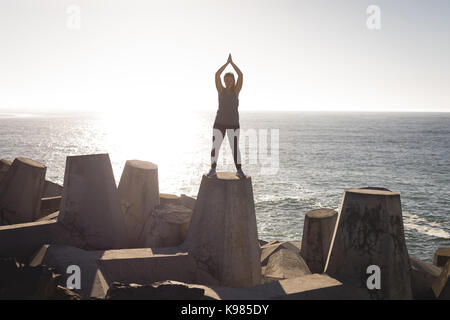 Junge Frau trainieren beim Stehen auf Felsen am Strand während der sonnigen Tag Stockfoto