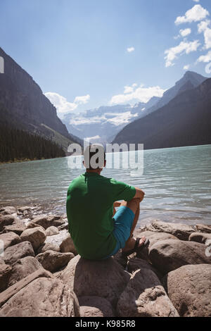 Rückansicht des Menschen sitzen in der Nähe von See an einem sonnigen Tag Stockfoto